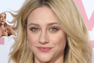 Lili Reinhart smiling on a red carpet, wearing a black dress with her hair styled in loose waves