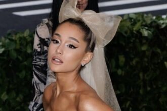 Ariana Grande in a concert outfit singing on stage with bright lights behind her