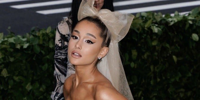 Ariana Grande in a concert outfit singing on stage with bright lights behind her