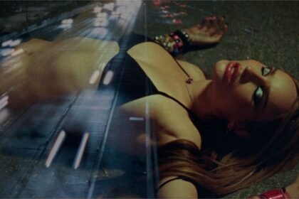 Kim Petras standing on a highway at night, wearing a dark outfit, with city lights in the background, as seen in the official 'Autobahn' music video.