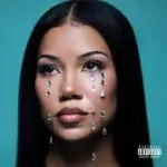 Jhené Aiko singing into a microphone on stage.