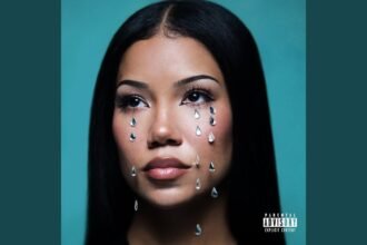 Jhené Aiko singing into a microphone on stage.