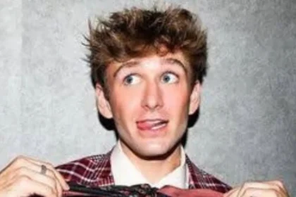 Carter Kench smiling while holding a phone, showing his TikTok video background with bright lights.
