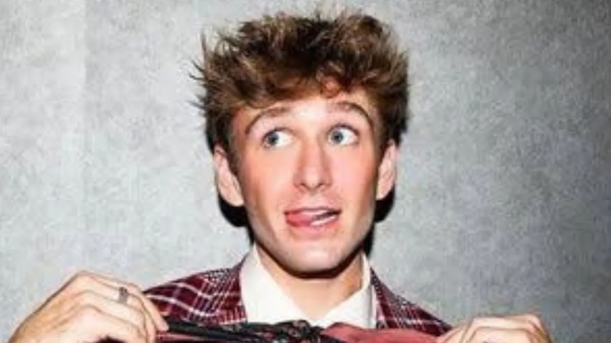 Carter Kench smiling while holding a phone, showing his TikTok video background with bright lights.