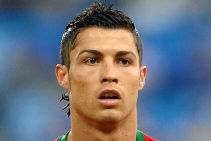 Cristiano Ronaldo in a soccer jersey raising his arms after scoring a goal, with a stadium crowd in the background.