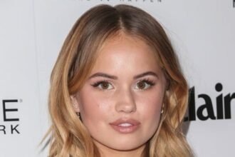 Debby Ryan smiling on a red carpet, wearing a casual outfit