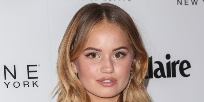 Debby Ryan smiling on a red carpet, wearing a casual outfit
