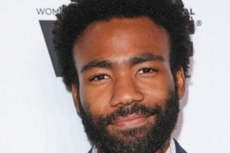 Donald Glover wearing a casual shirt, standing on a city street set while filming Atlanta.