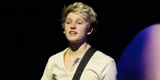 Drew Dirksen singing on stage with his band The Tide, holding a microphone, with bright stage lights behind him.