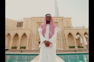 Royal MusiQ performing in the official video for DUMB & DUMBER (Intro), showing the artist in a studio setting with colorful lighting.
