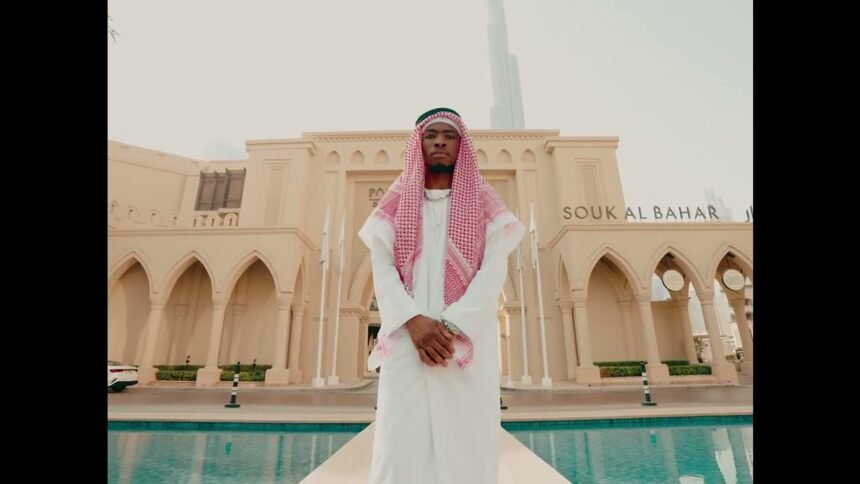 Royal MusiQ performing in the official video for DUMB & DUMBER (Intro), showing the artist in a studio setting with colorful lighting.