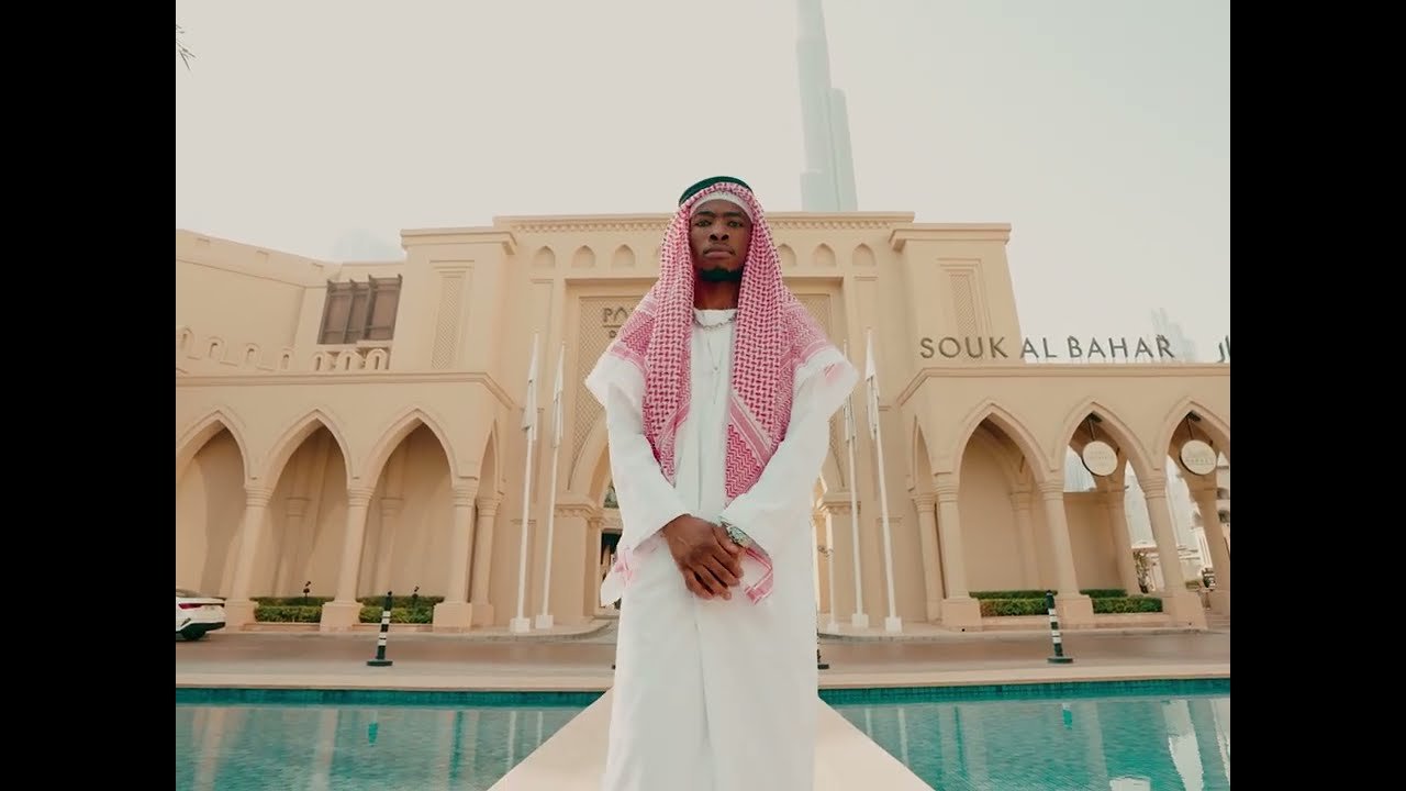 Royal MusiQ performing in the official video for DUMB & DUMBER (Intro), showing the artist in a studio setting with colorful lighting.