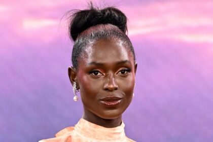 Jodie Turner-Smith wearing a black dress on a red carpet, smiling at cameras