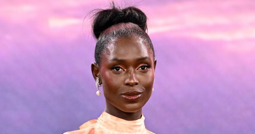 Jodie Turner-Smith wearing a black dress on a red carpet, smiling at cameras