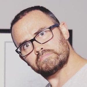 Jonathan Joly standing in his home studio, wearing a casual shirt, with a camera and lights behind him