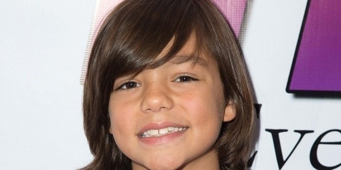 Malachi Barton smiling on a TV set, wearing casual clothing, with a background of lights and cameras