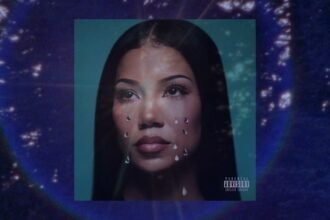 Jhené Aiko singing into a microphone under soft stage lights