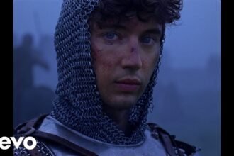 Troye Sivan dancing and smiling in a colorful outdoor setting during the 'Party' music video