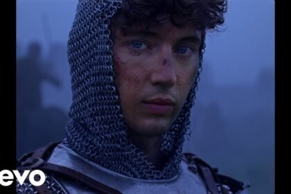 Troye Sivan dancing and smiling in a colorful outdoor setting during the 'Party' music video