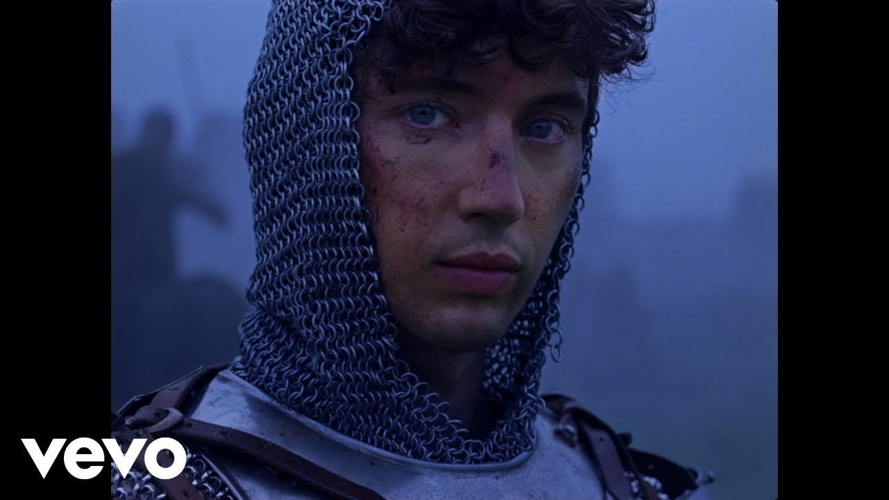 Troye Sivan dancing and smiling in a colorful outdoor setting during the 'Party' music video