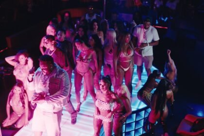 Screenshot from the official music video 'Rain' showing Tee Grizzley, Skilla Baby and Ashanti standing under street lights in rain.
