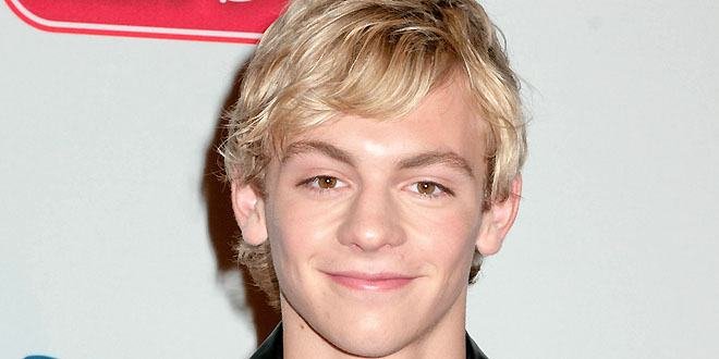 Ross Lynch sings and plays guitar on stage with his band The Driver Era, wearing a black jacket and smiling at the audience.