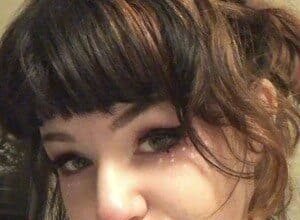 Emily, known as Stupid Ratgirl, smiling while holding her phone during a TikTok recording session