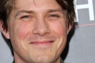 Taylor Hanson playing keyboard during a live concert, smiling and wearing a black shirt.