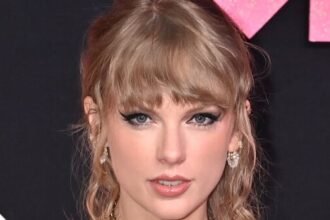 Taylor Swift smiling on a red carpet in 2025 wearing a glittering dress