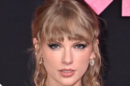Taylor Swift smiling on a red carpet in 2025 wearing a glittering dress