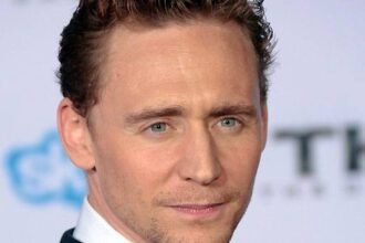 Tom Hiddleston wearing a dark suit, smiling on a red carpet