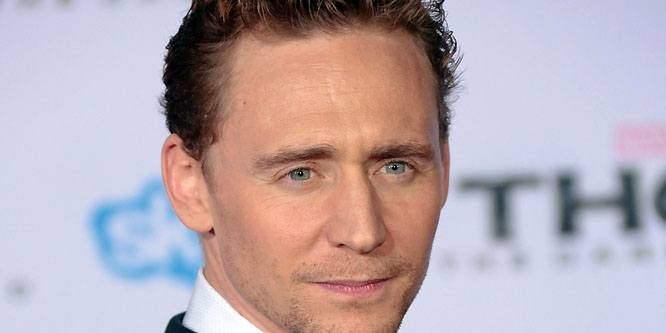 Tom Hiddleston wearing a dark suit, smiling on a red carpet