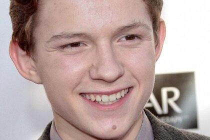 Tom Holland smiling in a suit at a movie premiere, with a backdrop of a city skyline