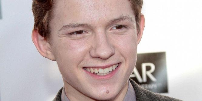 Tom Holland smiling in a suit at a movie premiere, with a backdrop of a city skyline