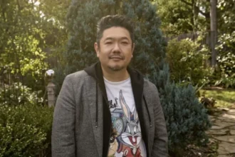 Eric Bauza smiling while holding a microphone at a Looney Tunes promotional event.