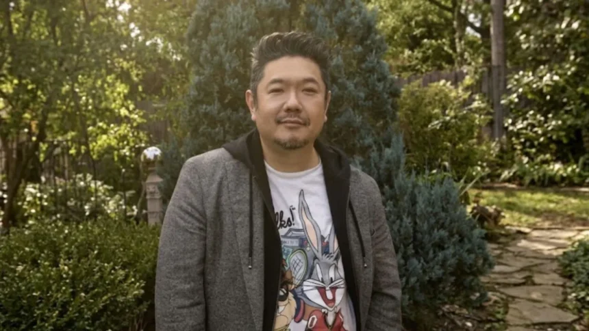 Eric Bauza smiling while holding a microphone at a Looney Tunes promotional event.