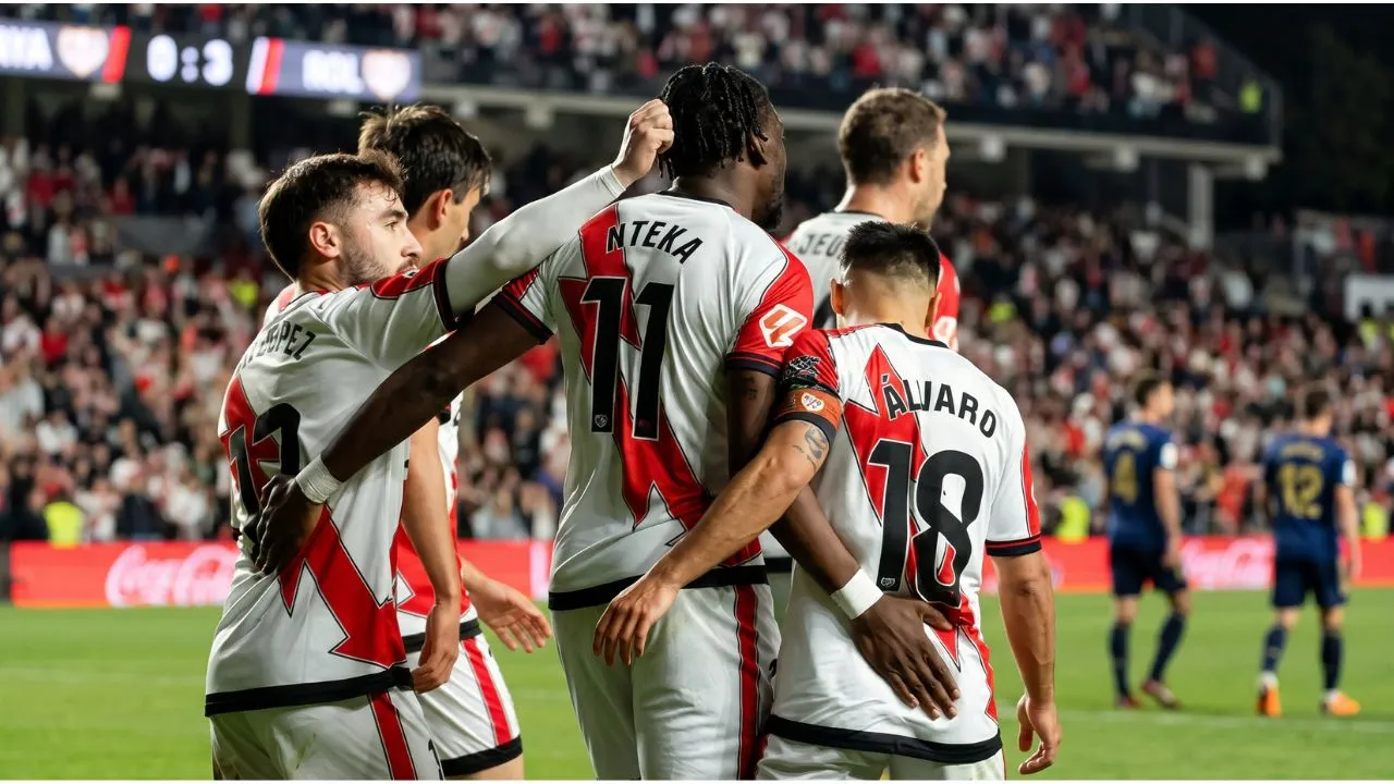 Rayo Vallecano players in red shirts and Elche players in white shirts standing on the pitch before the match at the Vallecas stadium.