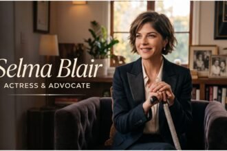 Selma Blair wearing a dark jacket, looking at the camera, with a neutral background