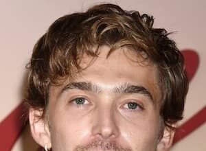 Austin Abrams smiling at a 2022 press event, wearing a black jacket.