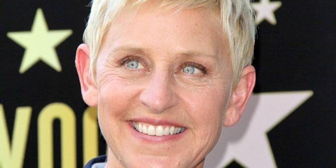 Ellen DeGeneres smiling on a red carpet, wearing a sleek black dress and holding a microphone during a talk‑show event.