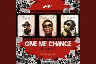 Winnerman on stage singing 'Give Me Chance (Remix)' with Sabushebu and Davido appearing on large screens behind him during a live performance.