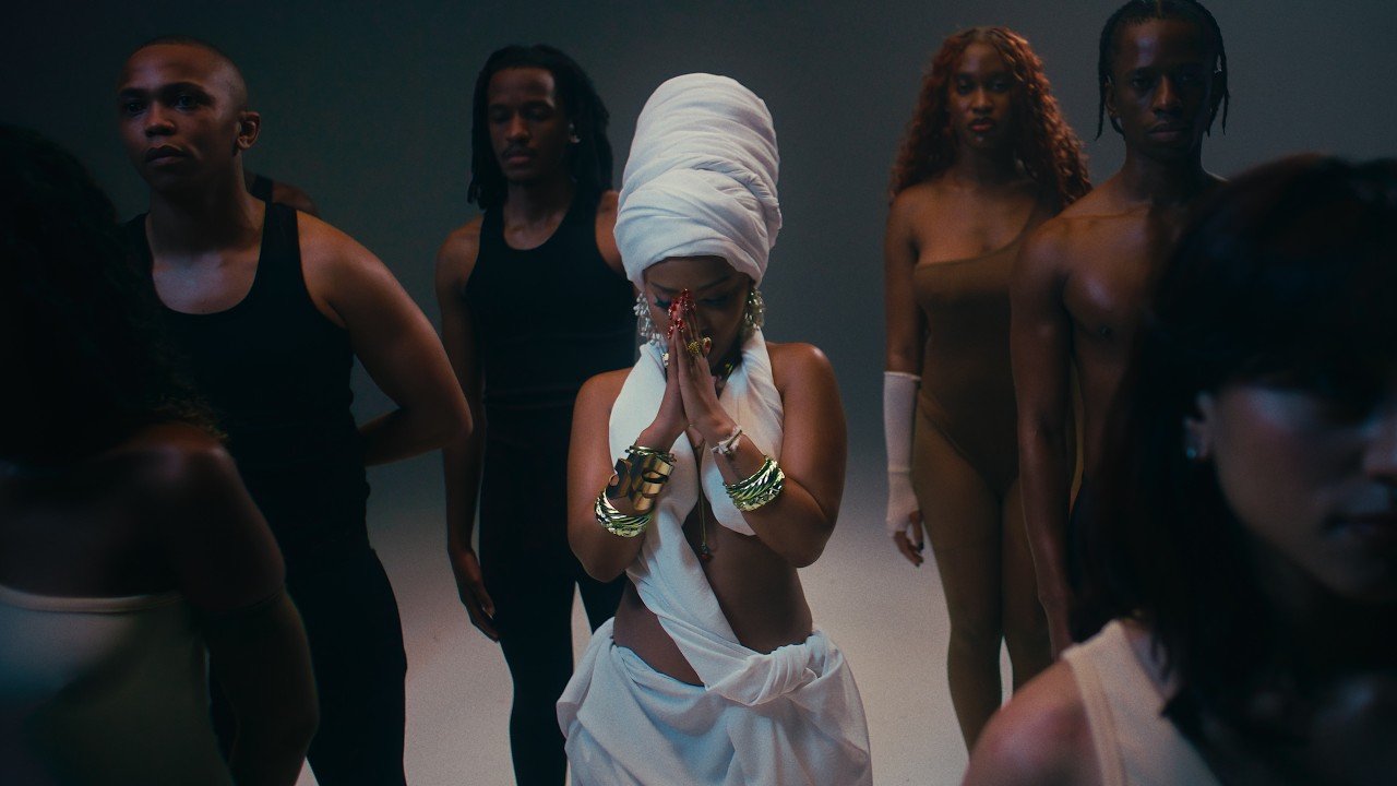 Zee Nxumalo, Dlala Thukzin, Funky QLA and TBO performing together on a stage set with bright lights in the Guqa (My Prayer) music video.
