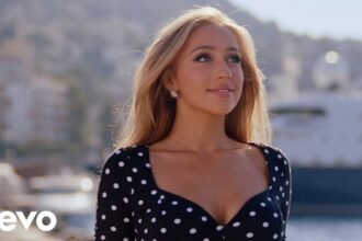 Tate McRae sings and dances in a bright studio set for the Housewife music video, wearing a sleek outfit with dynamic lighting.
