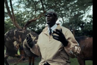 Bien performing in the 'I’ll Be Okay' music video, surrounded by dancers and stylized lighting, captured by cinematographer Dennis Odera.