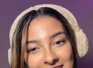 Portrait of Javeria Wasim, known as Jawbreaker Girl, standing in a bright studio with a TikTok logo backdrop, smiling after her viral jaw injury.