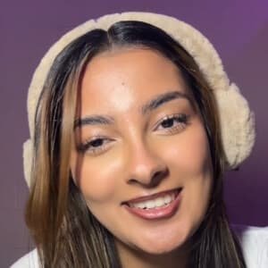 Portrait of Javeria Wasim, known as Jawbreaker Girl, standing in a bright studio with a TikTok logo backdrop, smiling after her viral jaw injury.
