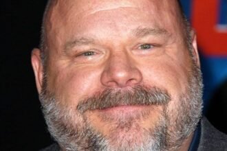 Kevin Chamberlin smiling on a stage with a theater curtain behind him