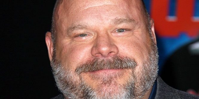 Kevin Chamberlin smiling on a stage with a theater curtain behind him