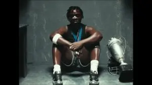 Kweku Smoke on stage singing Okwantunii, wearing a black jacket, with a microphone in hand, background lights.