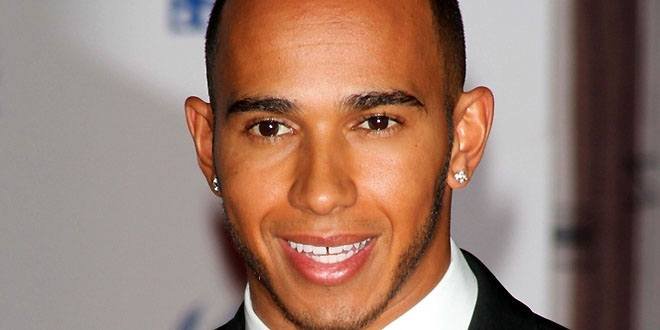 Lewis Hamilton wearing a Mercedes racing suit, smiling on the podium with a trophy and British flag in the background